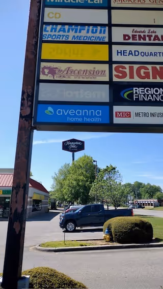 Tall outdoor signboard listing multiple businesses, including Aveanna Home Health, beside a parking lot.
