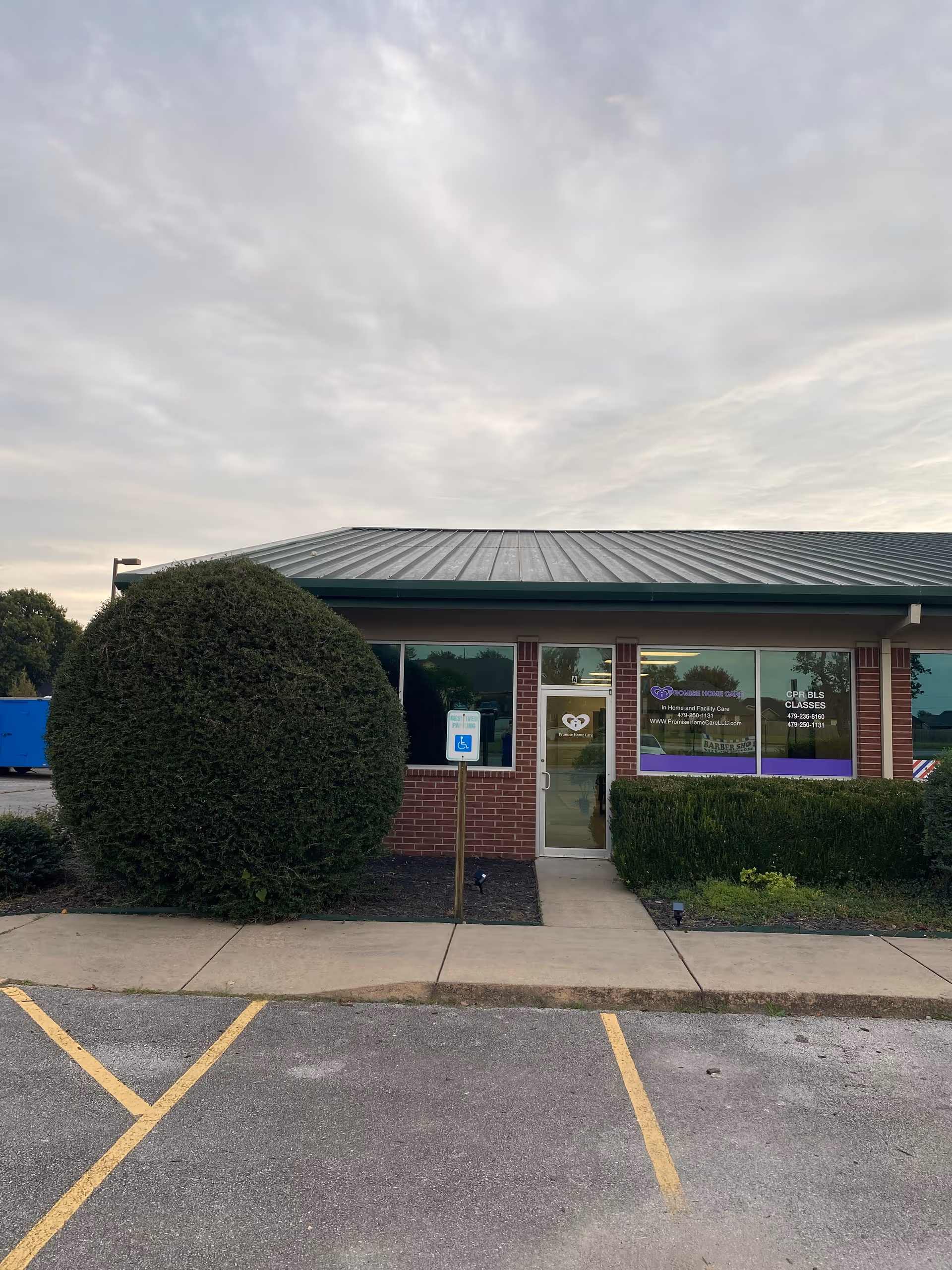 Front exterior of Promise Home Care and Transportation building with a large shrub and handicap sign.