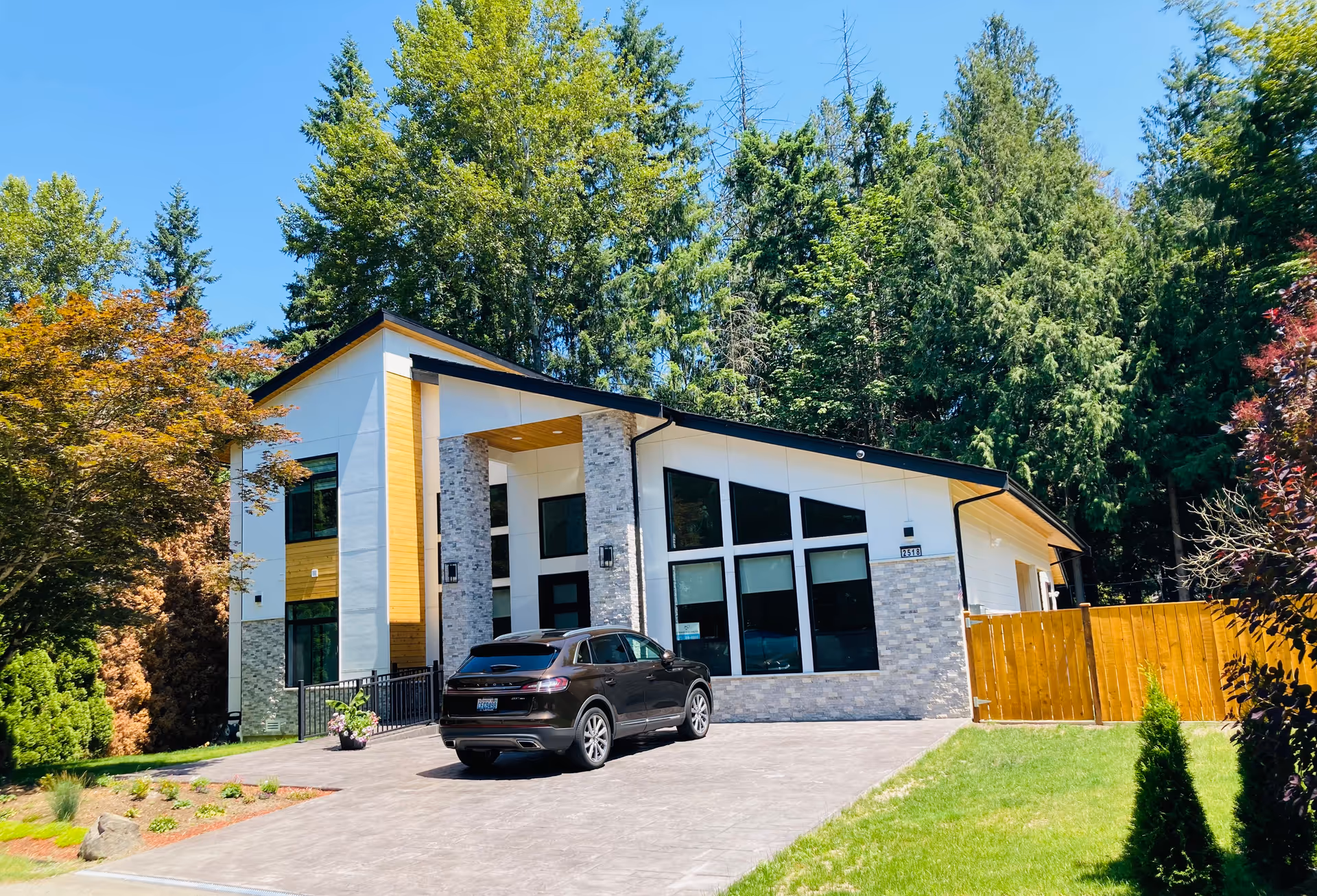 Modern single-story senior living facility exterior with large windows, driveway, and trees.