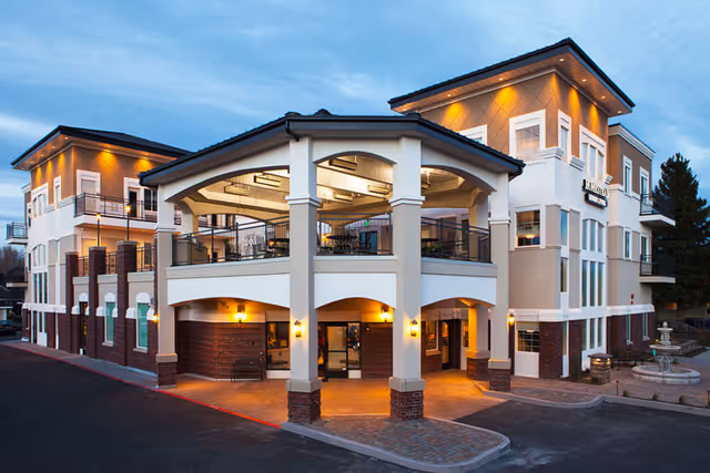 Three-story assisted living building with a covered porte-cochère entrance and upper-level outdoor seating at dusk.