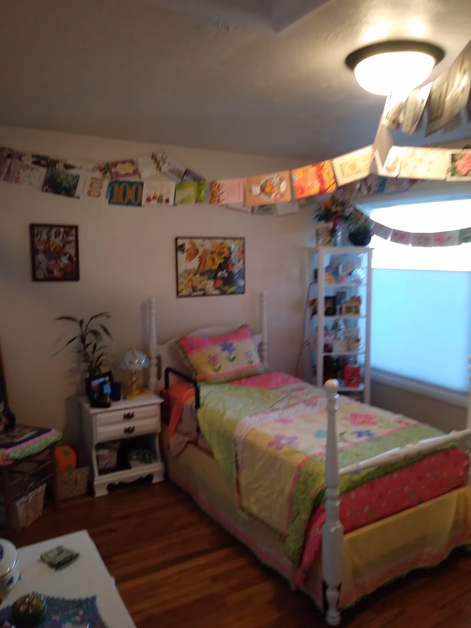A cozy bedroom with a white four-poster bed, colorful quilt, shelves, and banners.