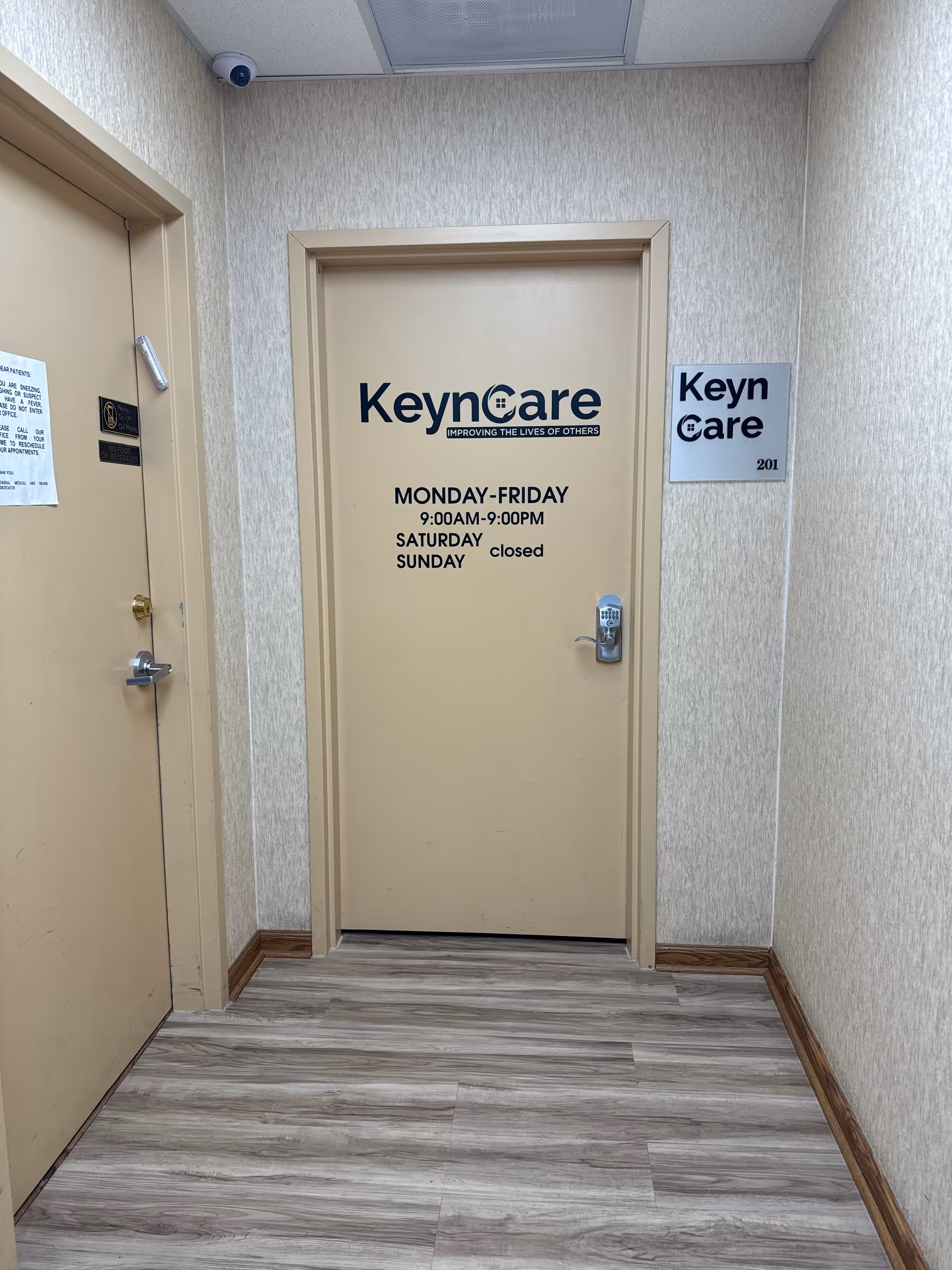 Narrow beige hallway with a KeynCare door and sign in a senior living facility.