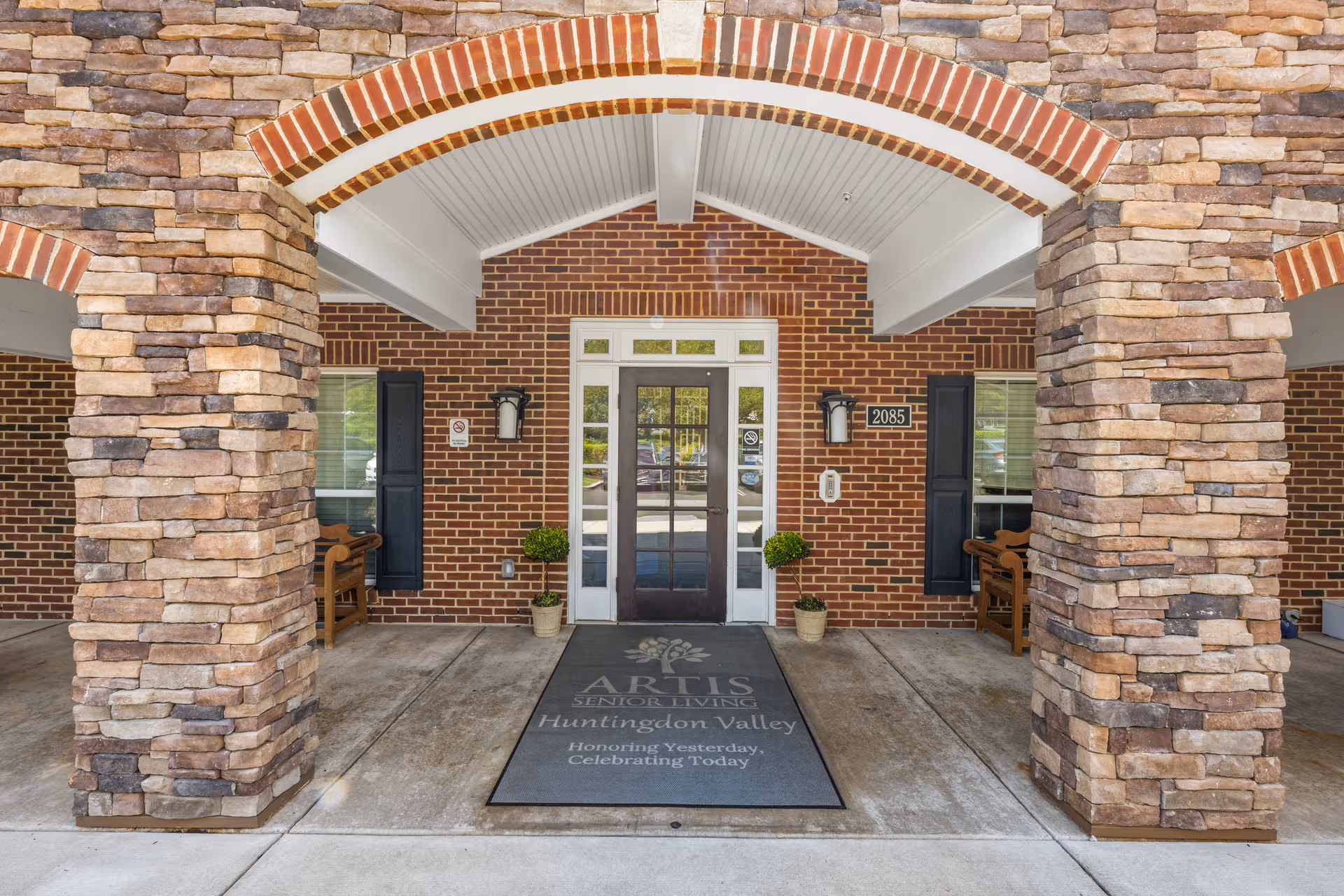 Brick-front entrance with stone pillars and a mat reading Artis Senior Living Huntingdon Valley