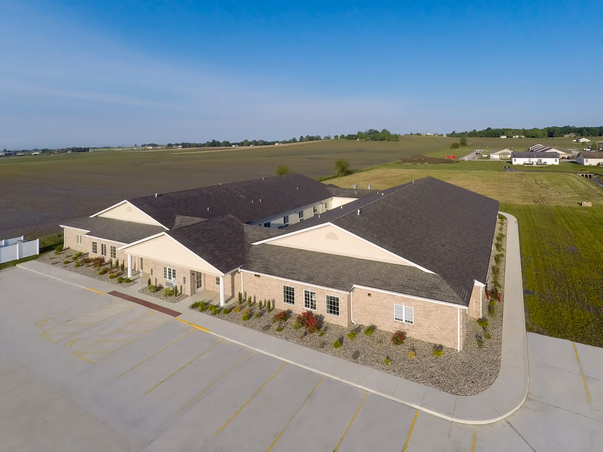 Aerial view of a single-story brick senior living facility with surrounding fields and parking.