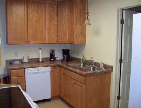 Kitchen area with wooden cabinets, sink, dishwasher, and countertop appliances in a senior facility.
