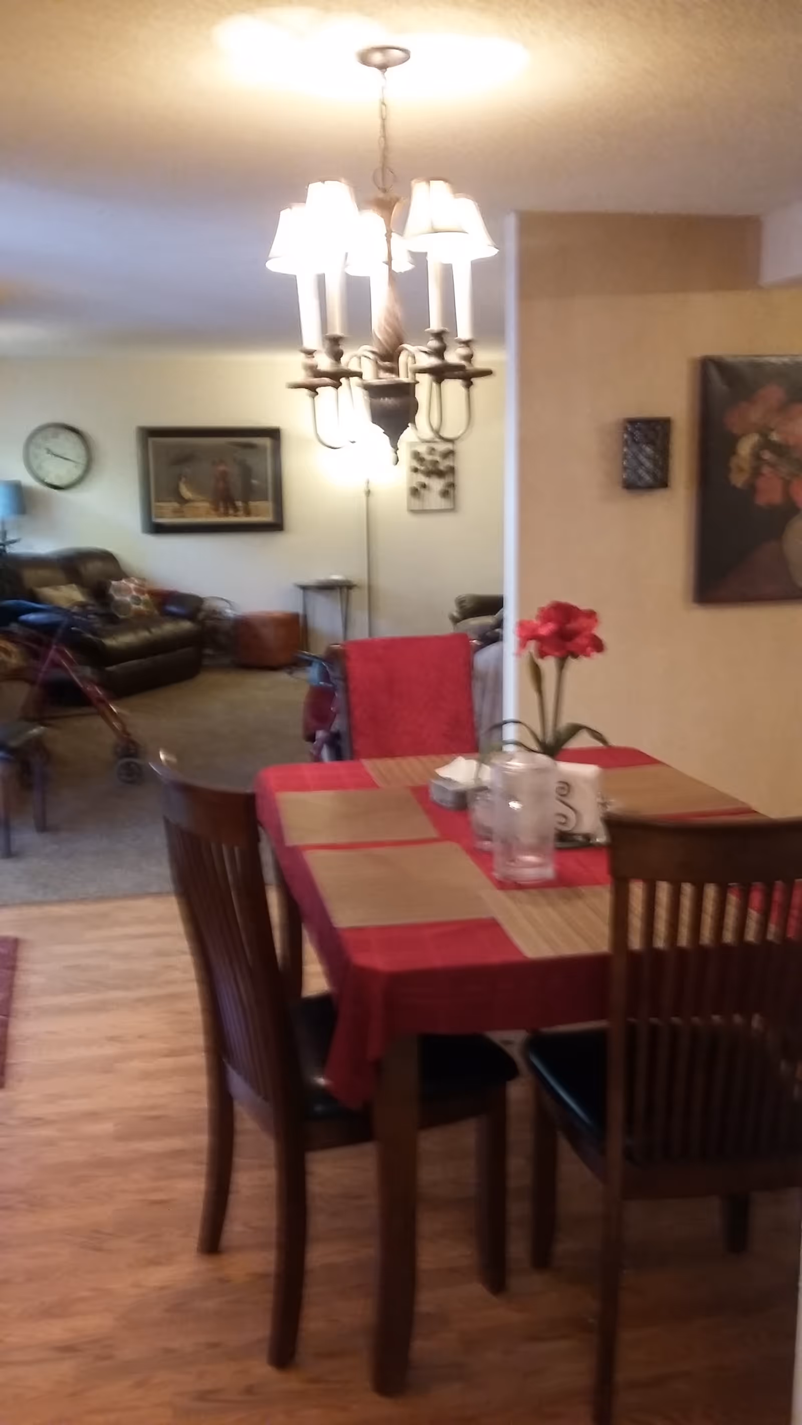 Allen's Adult Family Home II dining room with wooden table, red plaid tablecloth, chandelier, and flowers.