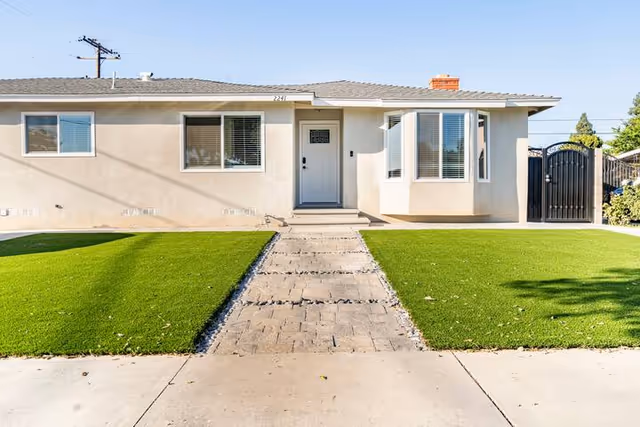 Front view of a single-story beige residential building with a walkway and green lawn