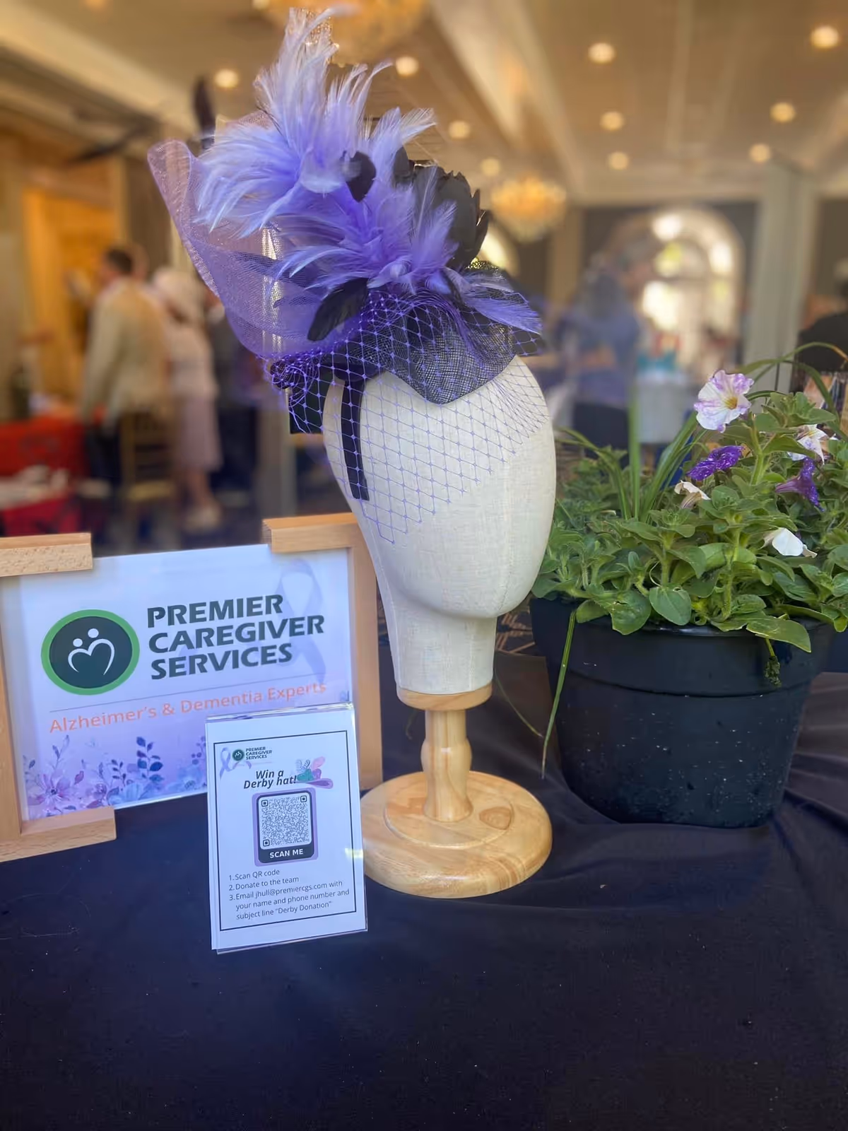 Decorative mannequin head with purple feathered hat beside Premier Caregiver Services sign on display table.