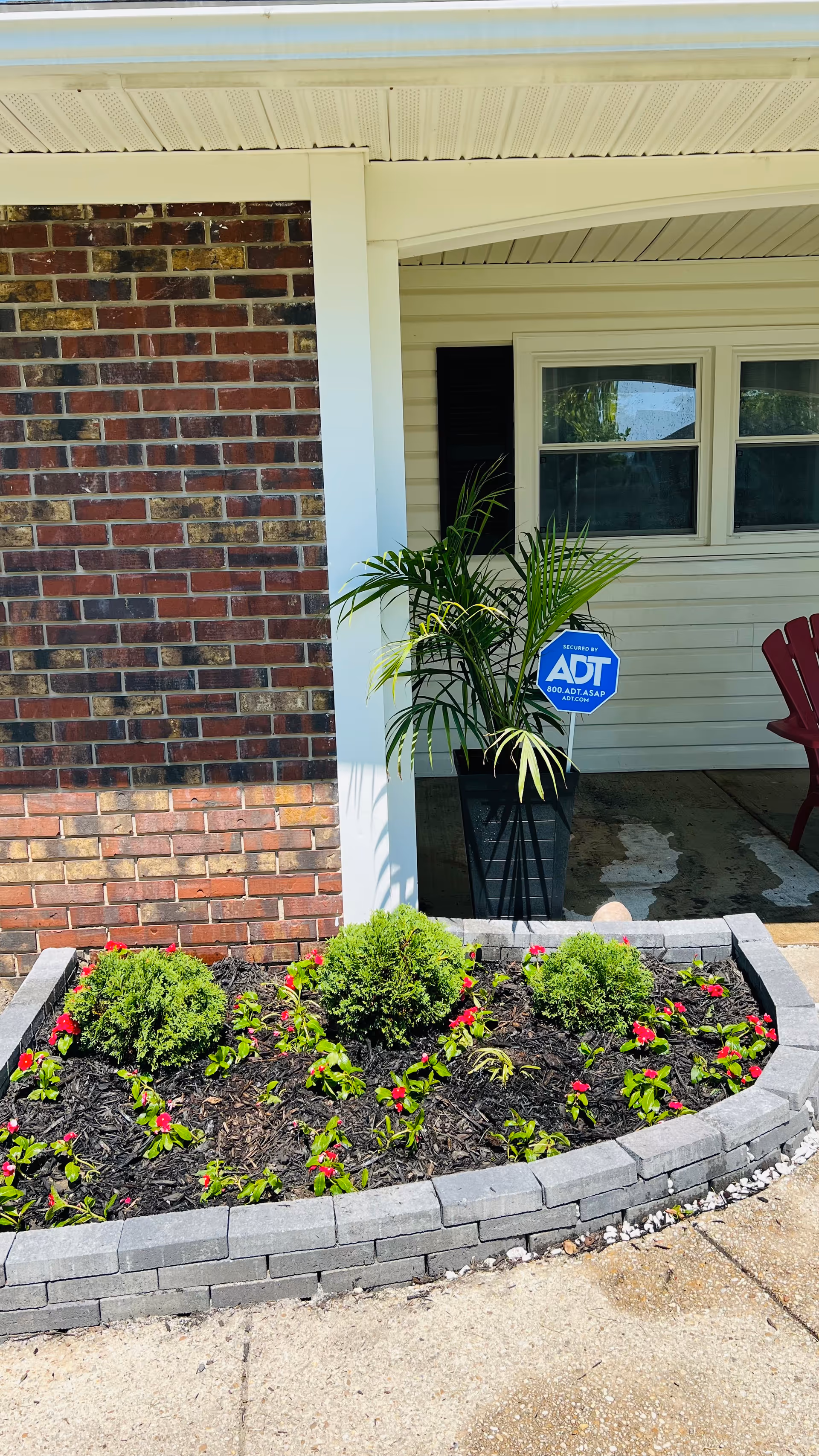 Front entrance of a senior living house with brick wall, plants, and an ADT security sign.