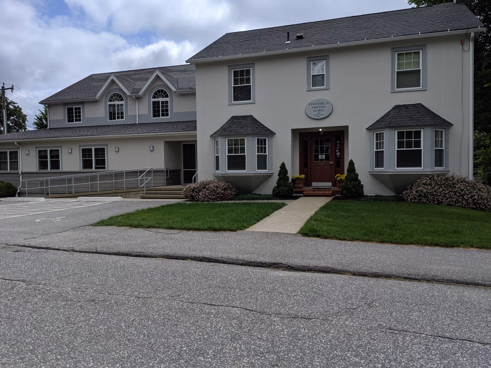 Front view of a white two-story senior care building with entrance sign and landscaping