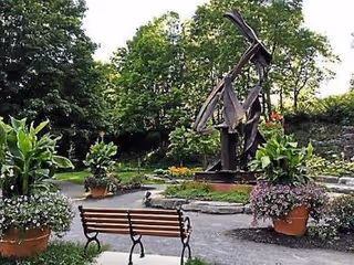 A garden courtyard with a wooden bench, potted plants, and a metal sculpture.