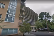 Exterior view of Holladay Park Plaza showing balconies, trees, and parked cars.