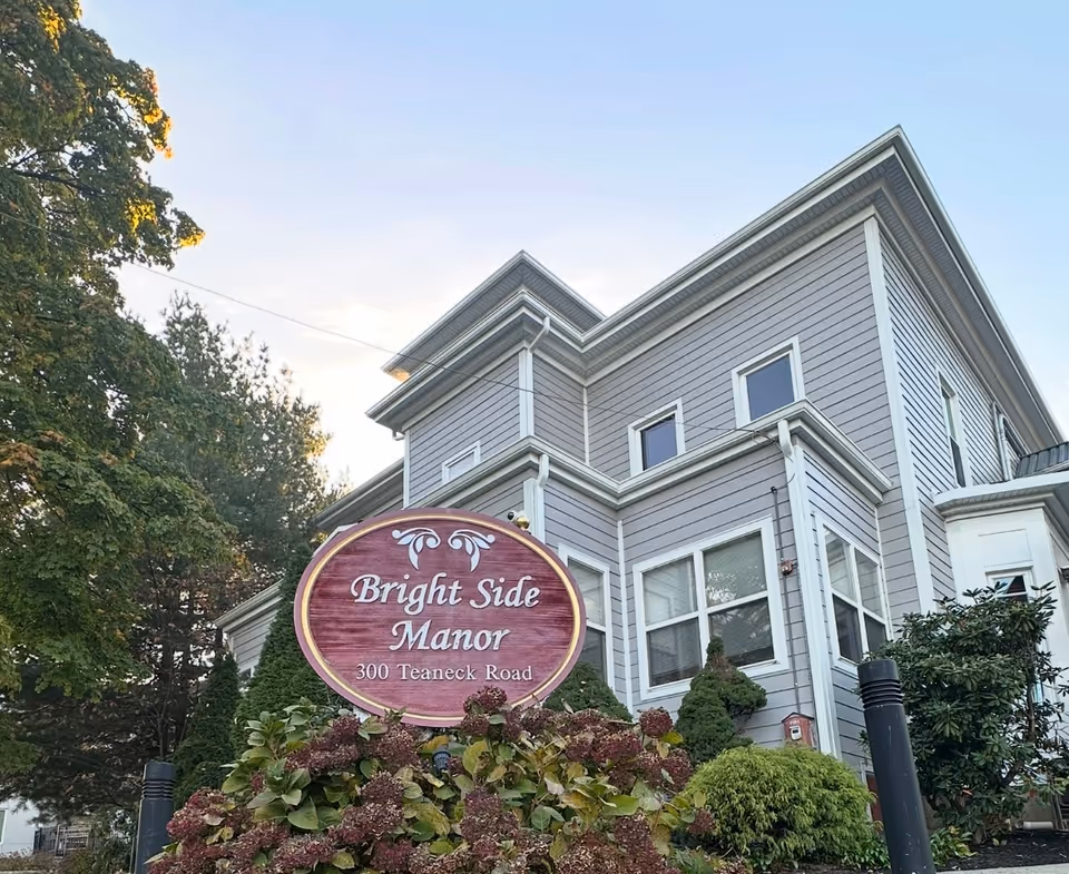 Exterior view of Bright Side Manor building with a round maroon sign in front