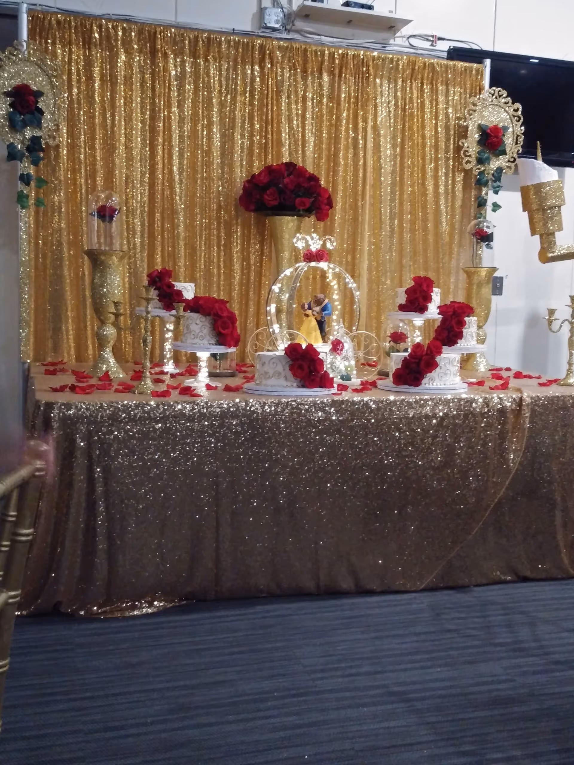 Gold-sequin dessert table with red roses and wedding cake displays indoors