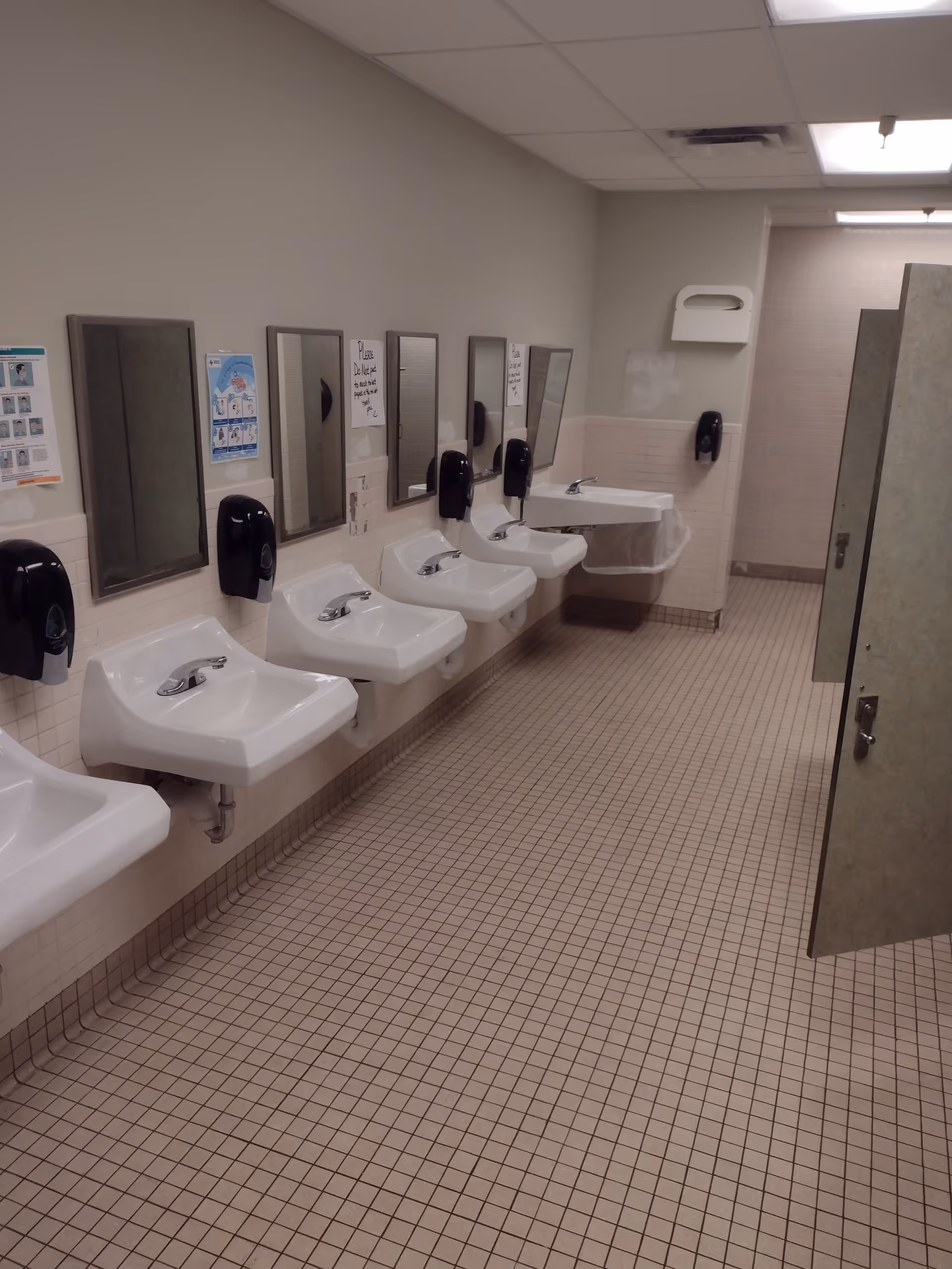 Row of sinks with mirrors and hand dryers in a tiled bathroom.