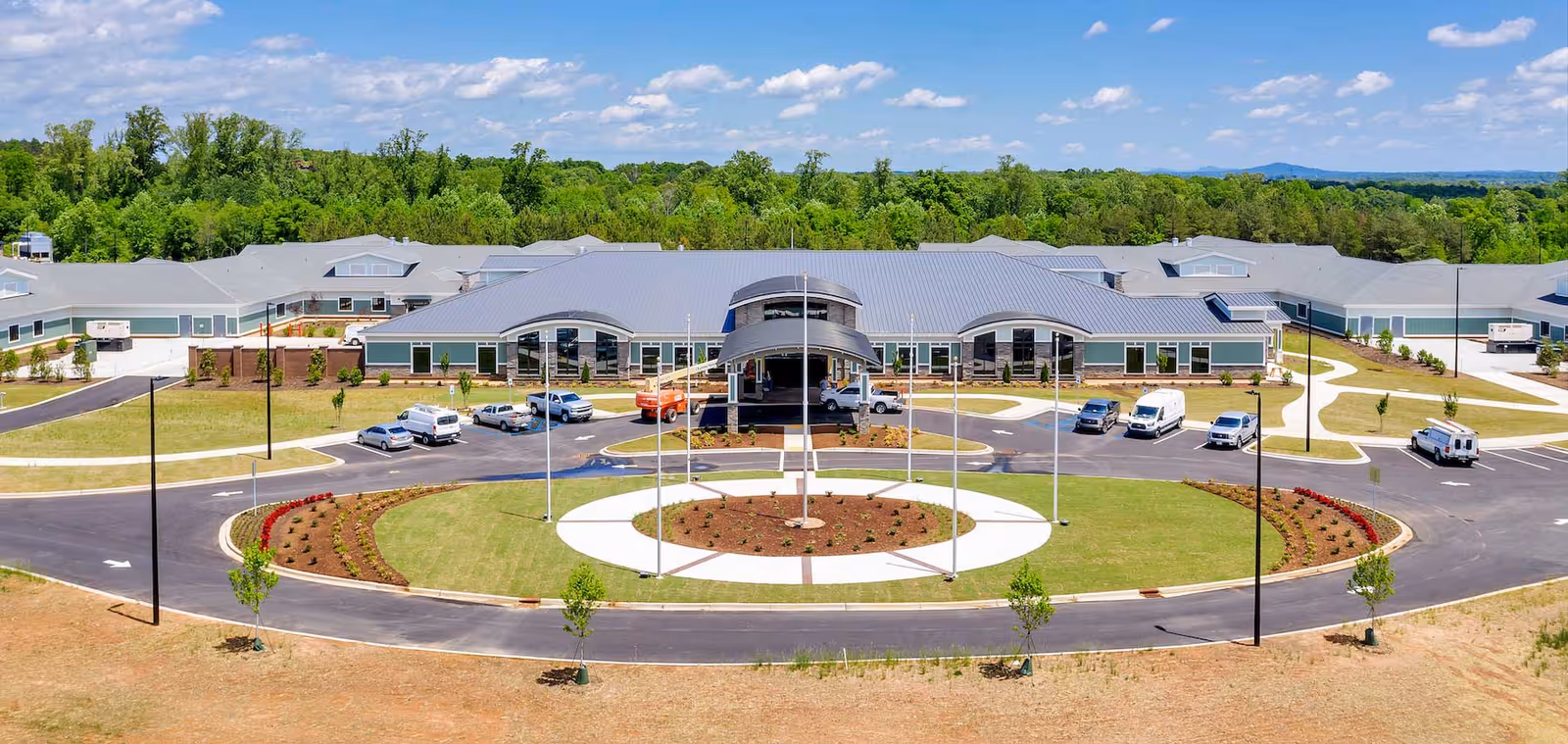 A large senior living facility with a circular driveway, front entrance, parked cars, and landscaped grounds.