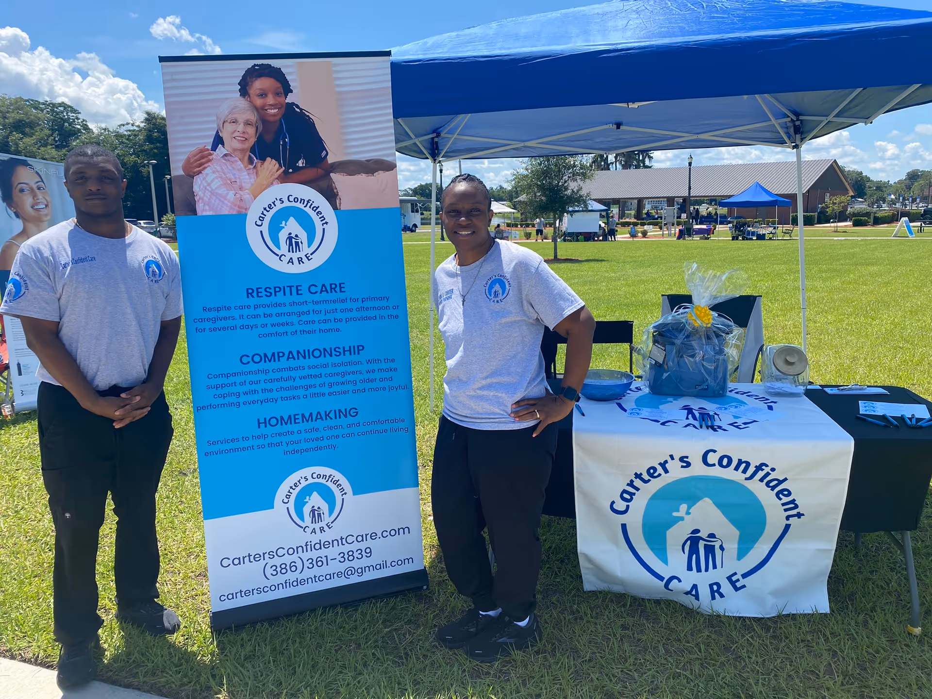 Two staff members stand beside a Carter's Confident Care banner under a blue canopy outdoors.