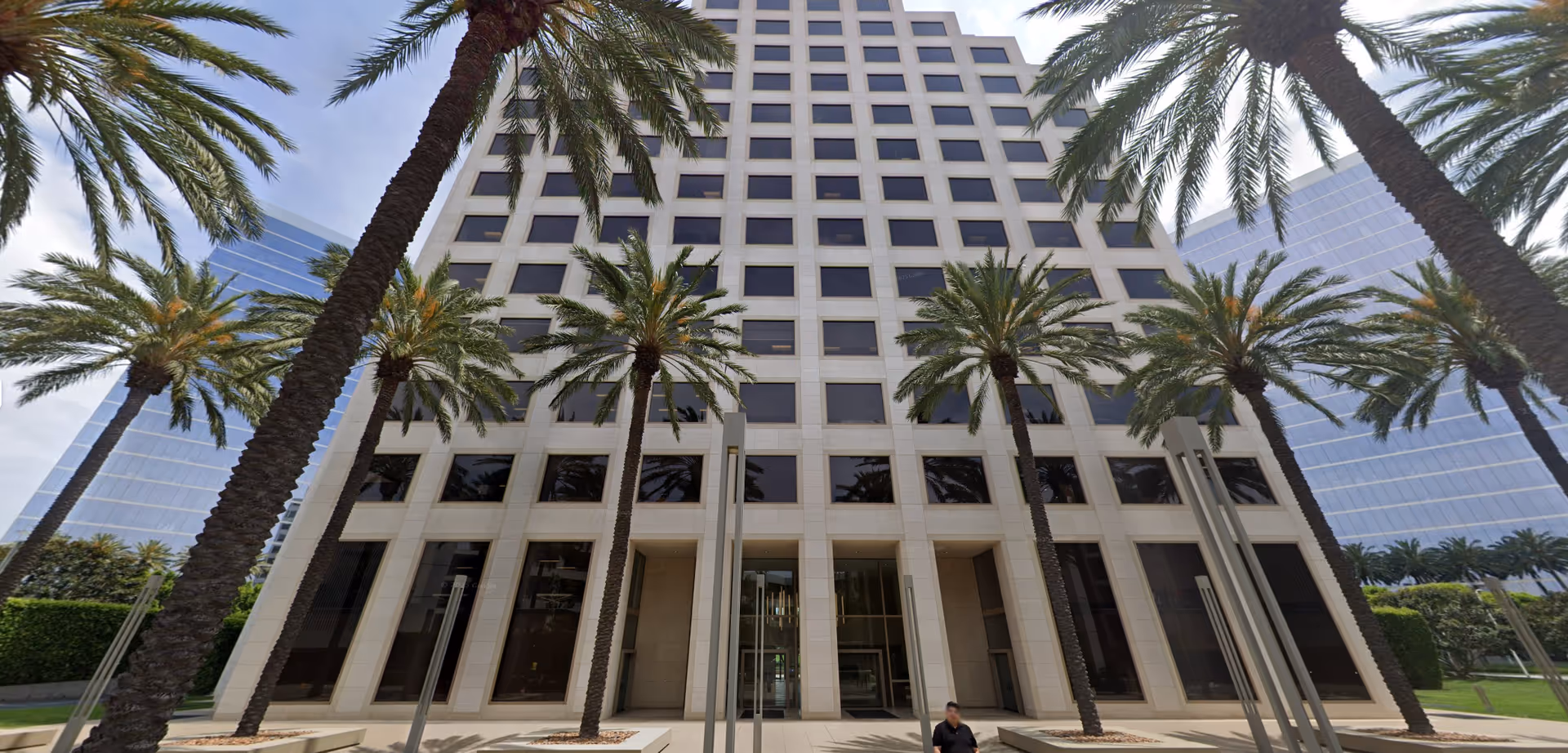 Exterior view of a tall modern building with palm trees and glass windows.