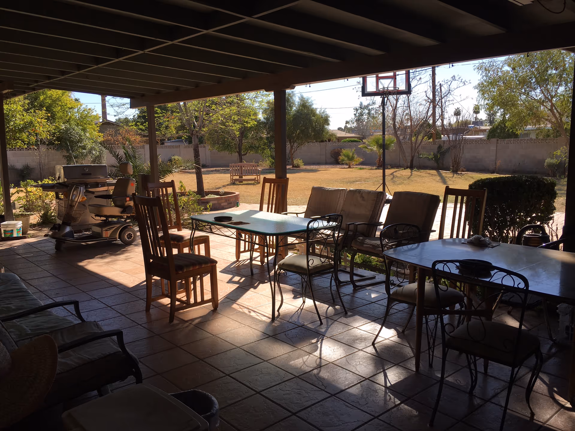 Covered outdoor patio with seating, a grill, and a yard with trees.
