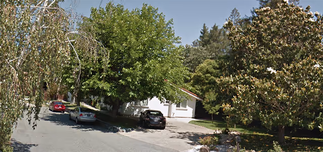 Exterior view of a small rest home with trees and parked cars.