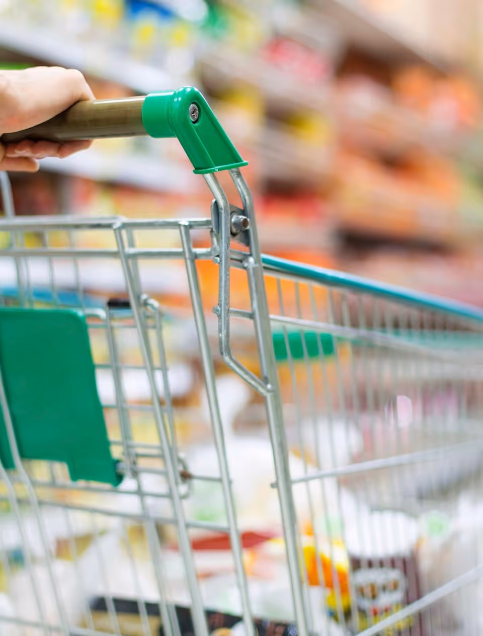 Close-up of a green-handled shopping cart in a grocery store aisle.