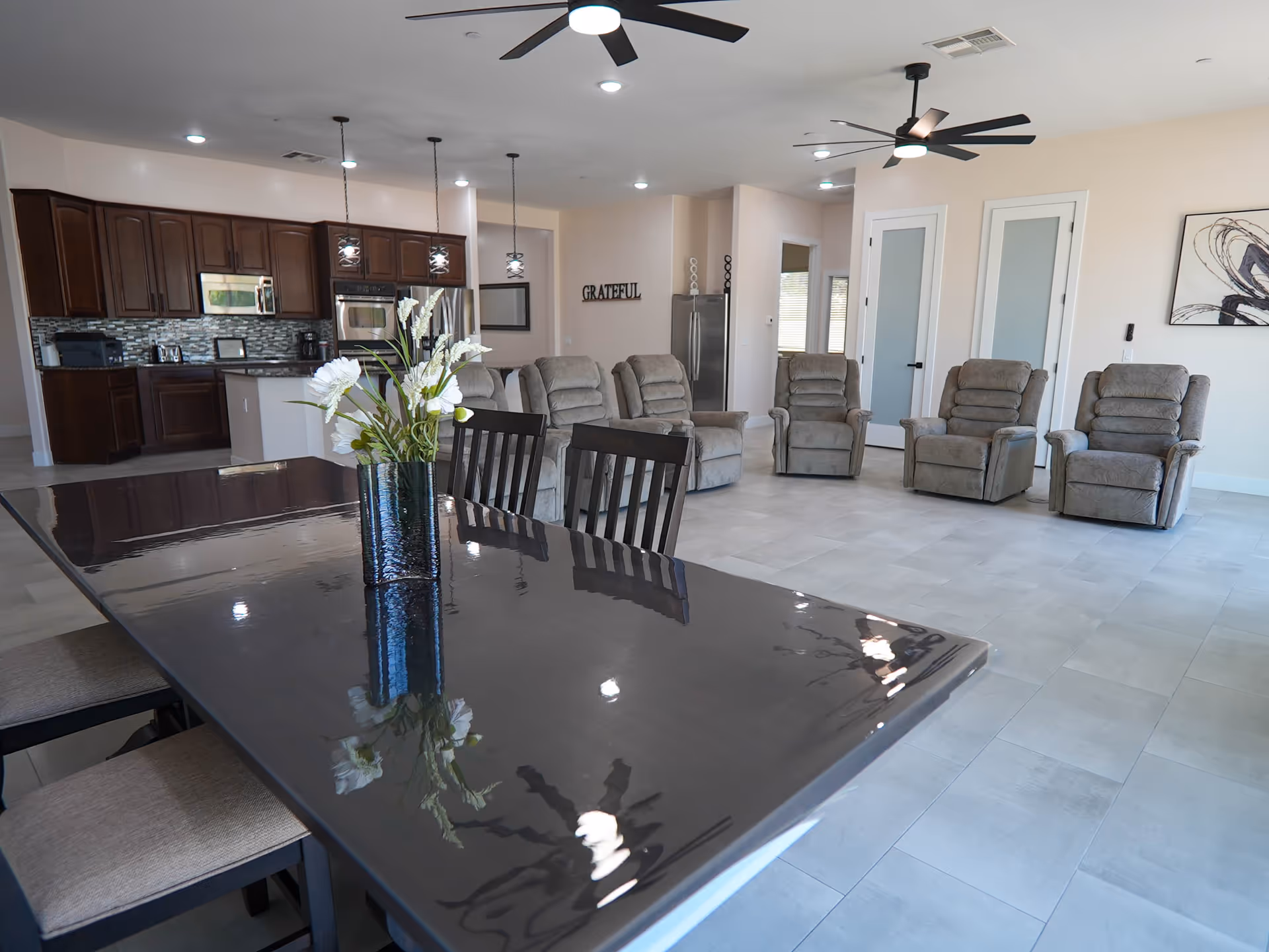 Open concept communal area featuring a glossy dining table, vase, and recliner seating.