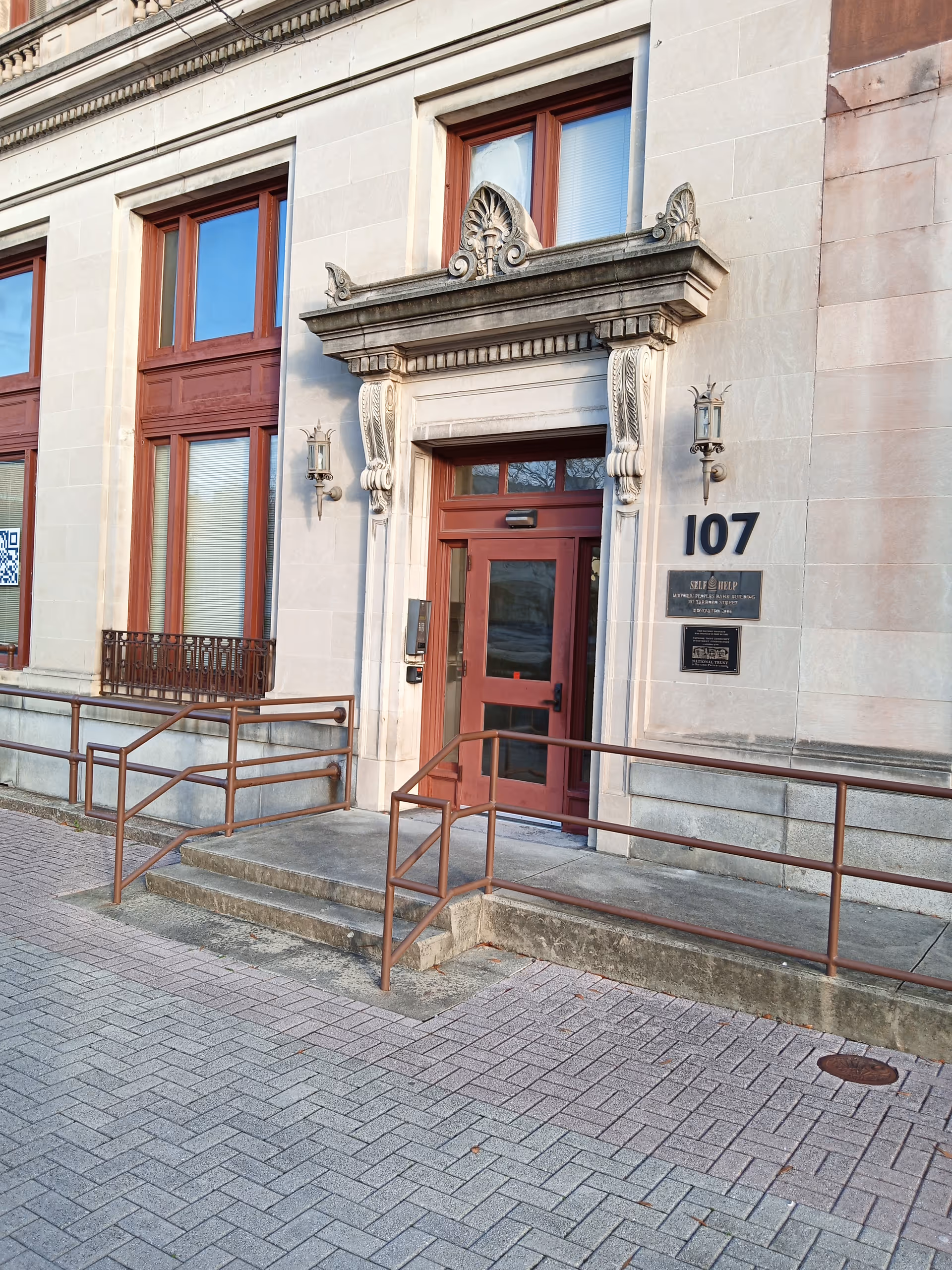 Stone building entrance with red doors, ornate doorway, and accessibility ramps.