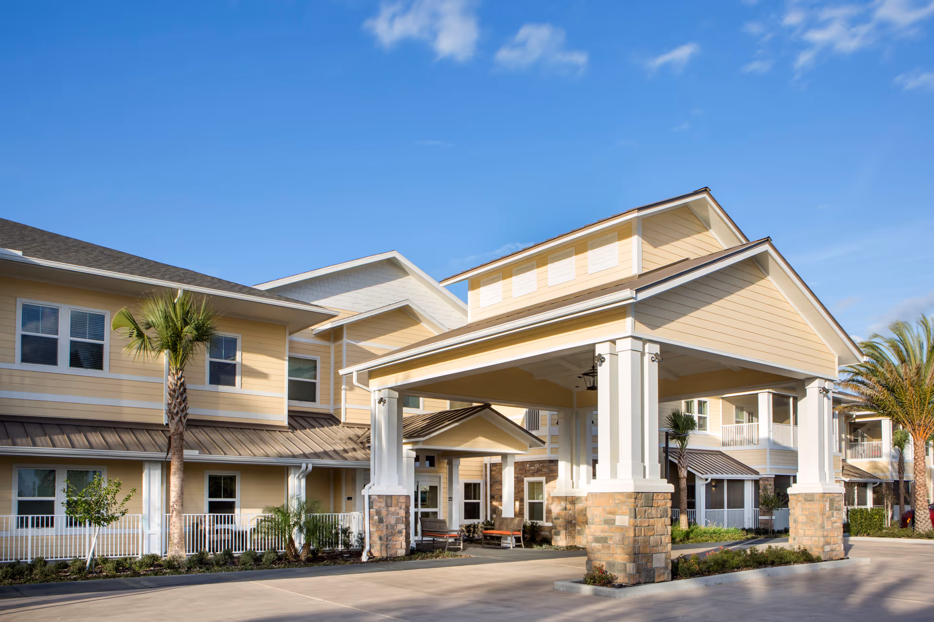 Exterior view of The Summit of Winter Garden facility showing a covered entrance with stone pillars and beige siding under a clear blue sky. Palm trees and landscaping are visible around the building.