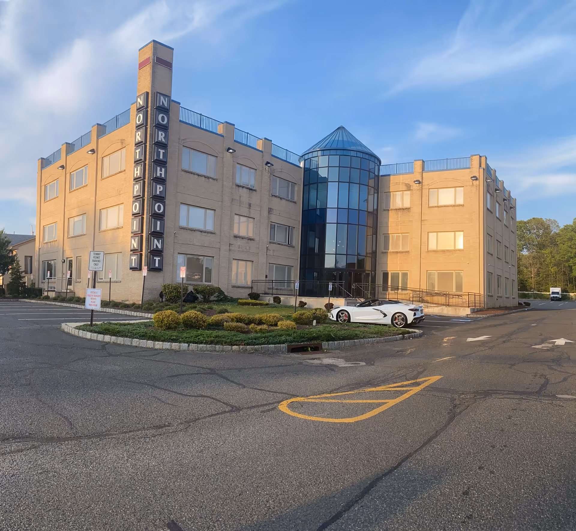 Front view of a tan brick senior living building with a glass entrance and parking.