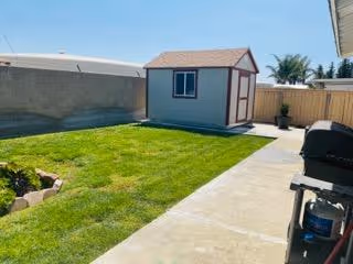 Backyard area of Dove Tree Manor with a small shed, lawn, and grill.