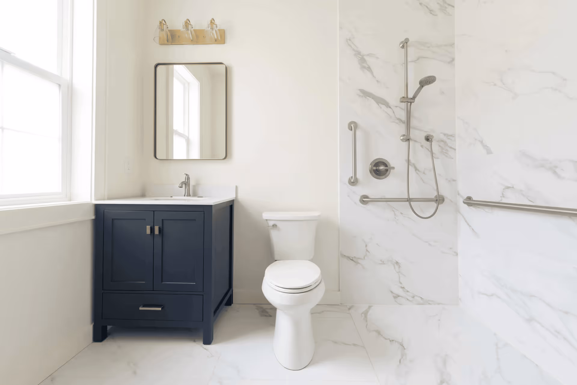 Bright bathroom with navy vanity, toilet, and marble tiled shower.