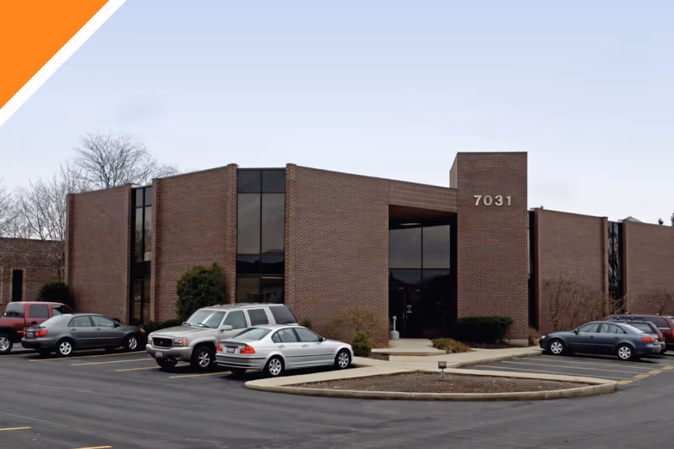 Brick building with a glass entrance, marked 7031, and a parking lot in front.
