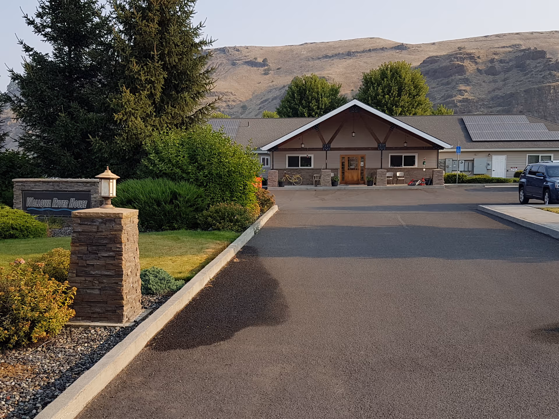 Sunlit front view of Wallowa River House entrance with sign and mountains