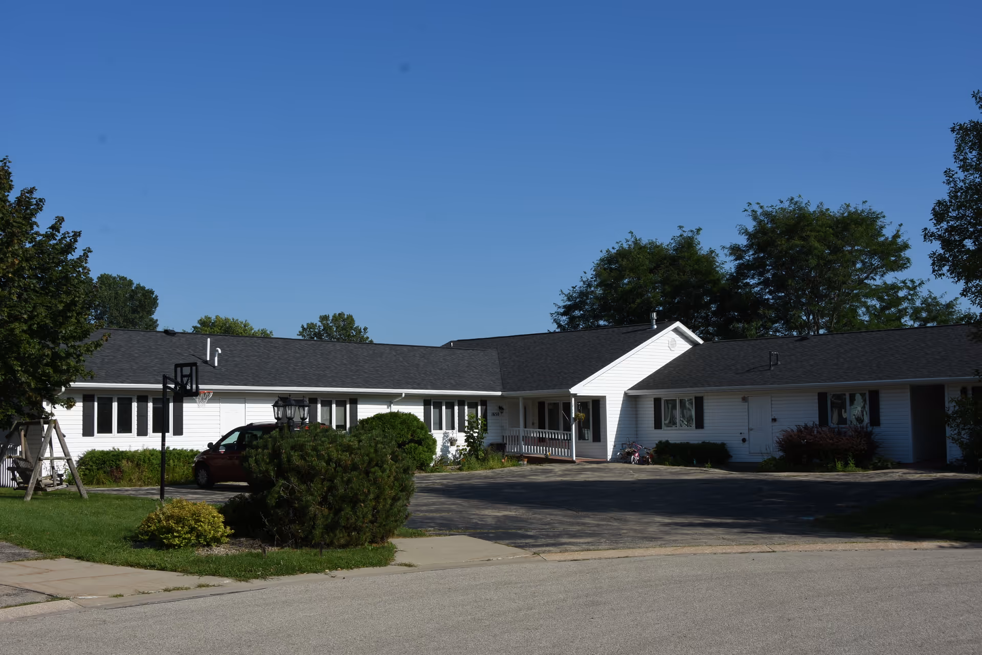 White, single-story senior living facility exterior with a central entrance and shrubbery.