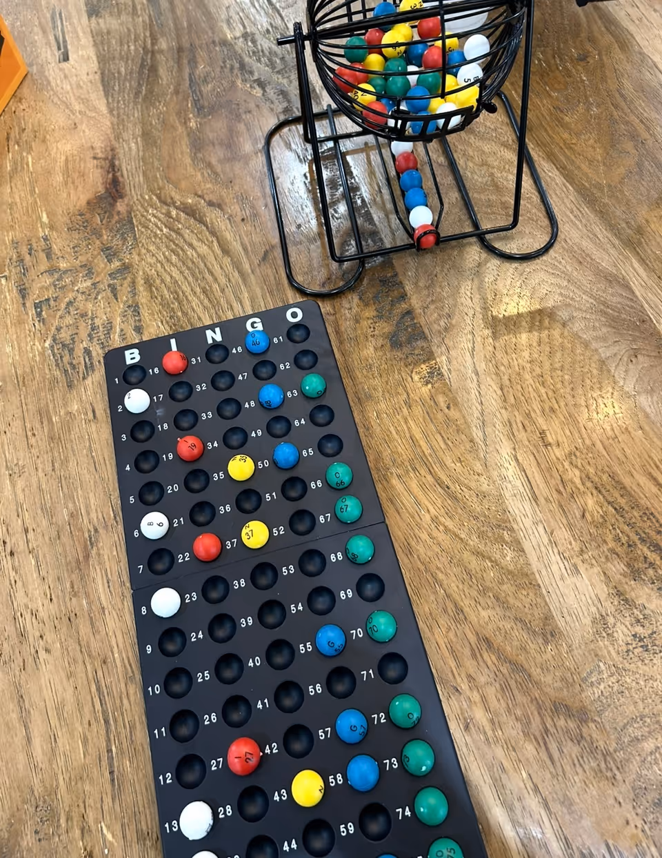 Indoor wooden floor with a bingo board, ball cage, and scattered colorful balls.