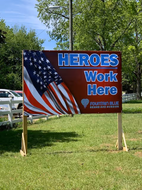 Outdoor sign on grass reading HEROES Work Here for Fountain Blue Rehab and Nursing
