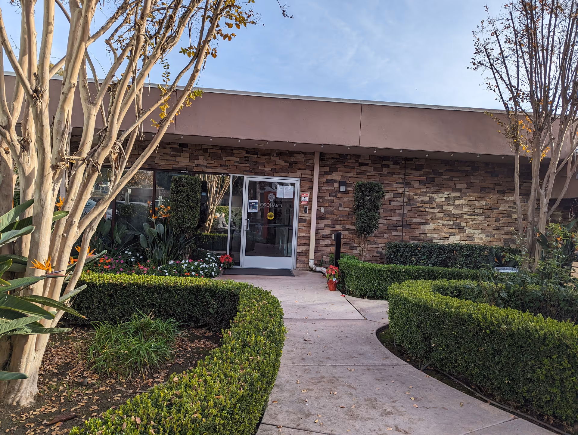 Brick exterior of a senior care facility with manicured hedges and glass entrance door.