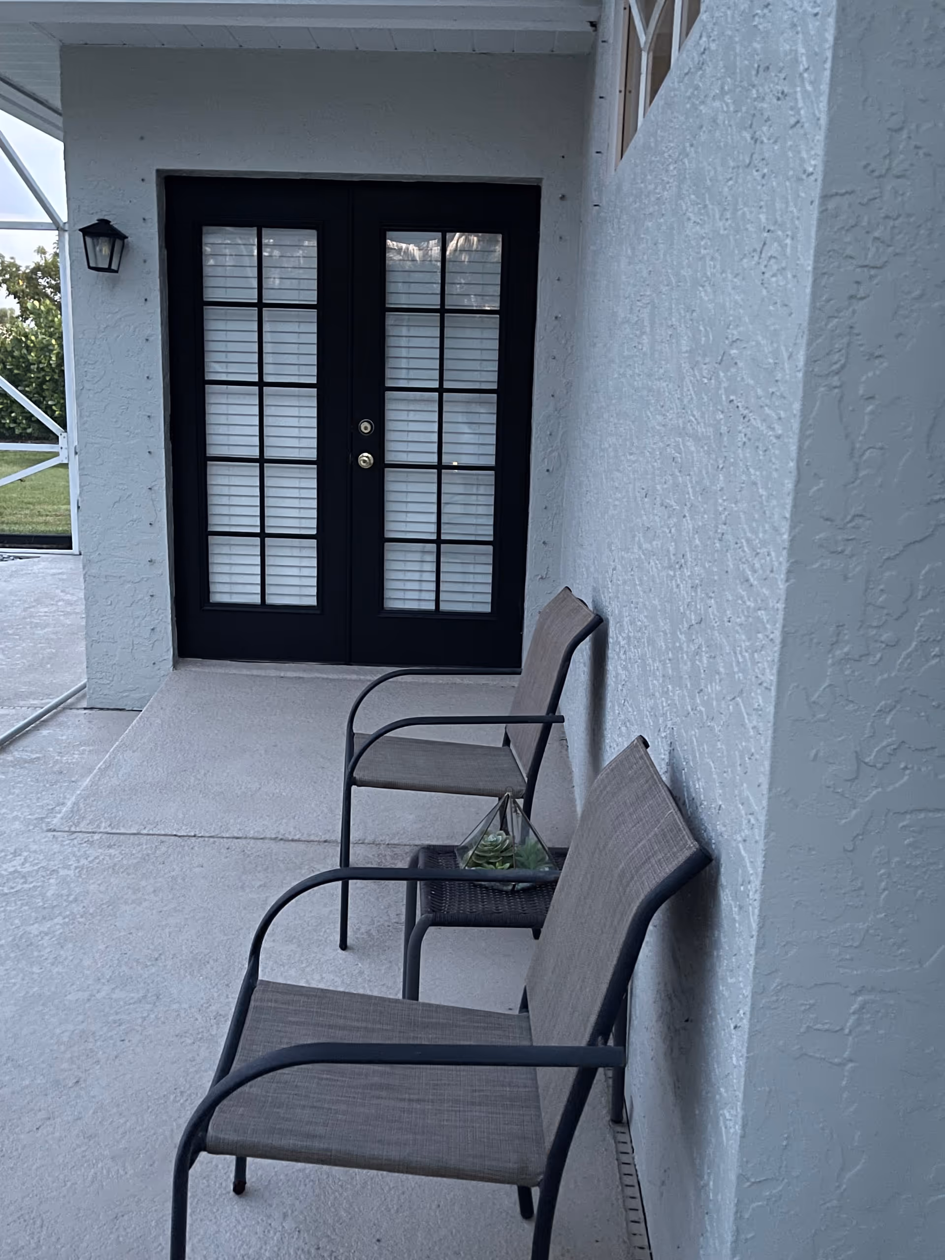 Outdoor porch with two beige chairs beside a black-framed double door entrance