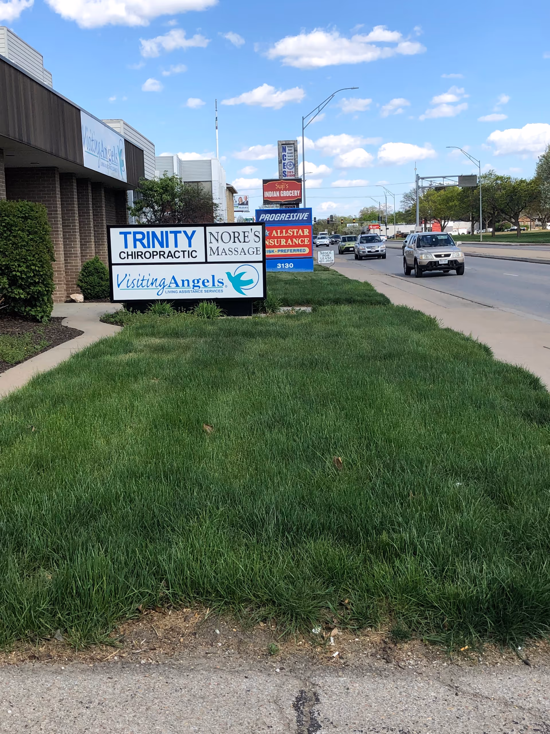 Exterior view of a grassy lawn with business signs, including Visiting Angels, along the street.