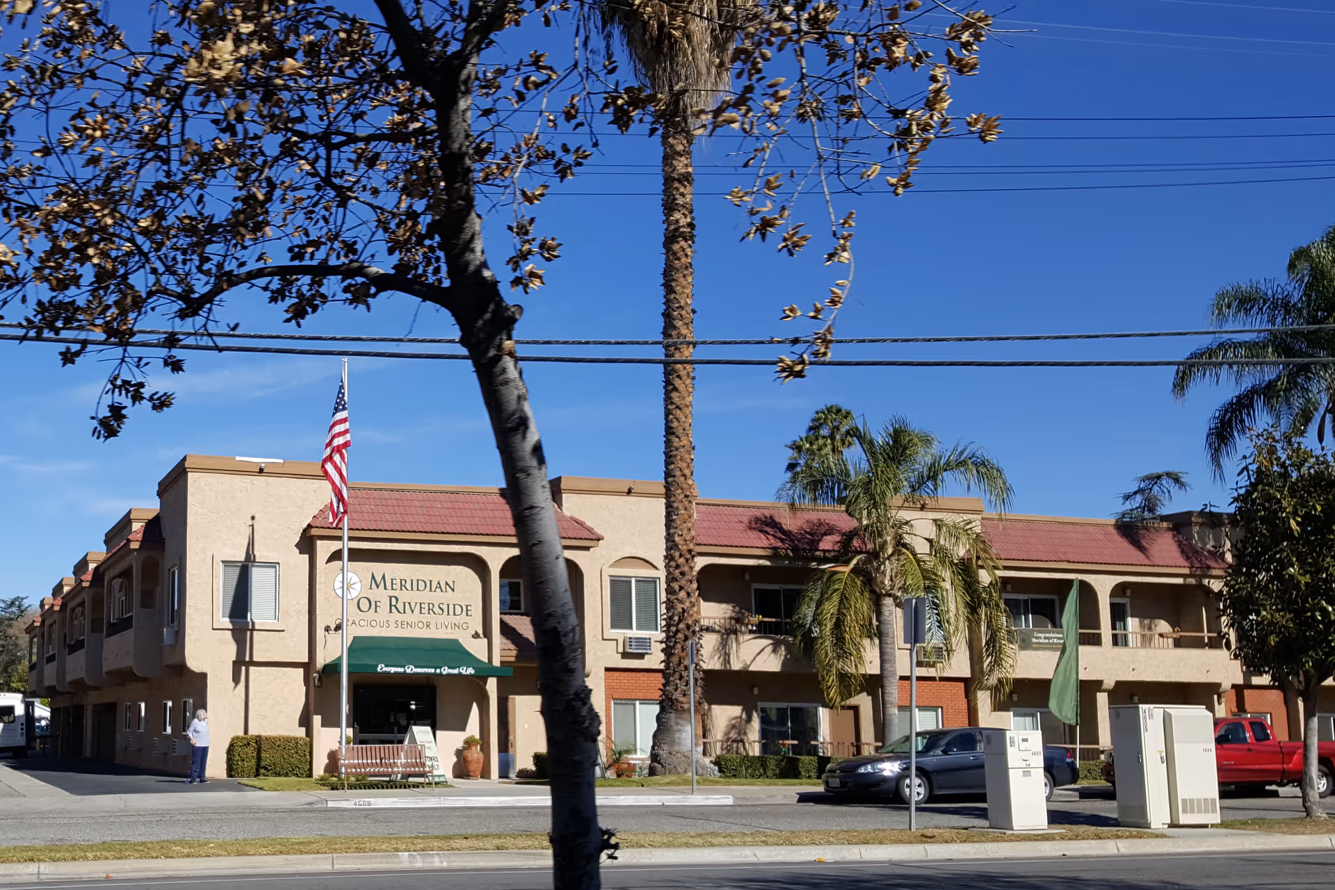 Front view of Meridian of Riverside senior living building with palm trees.
