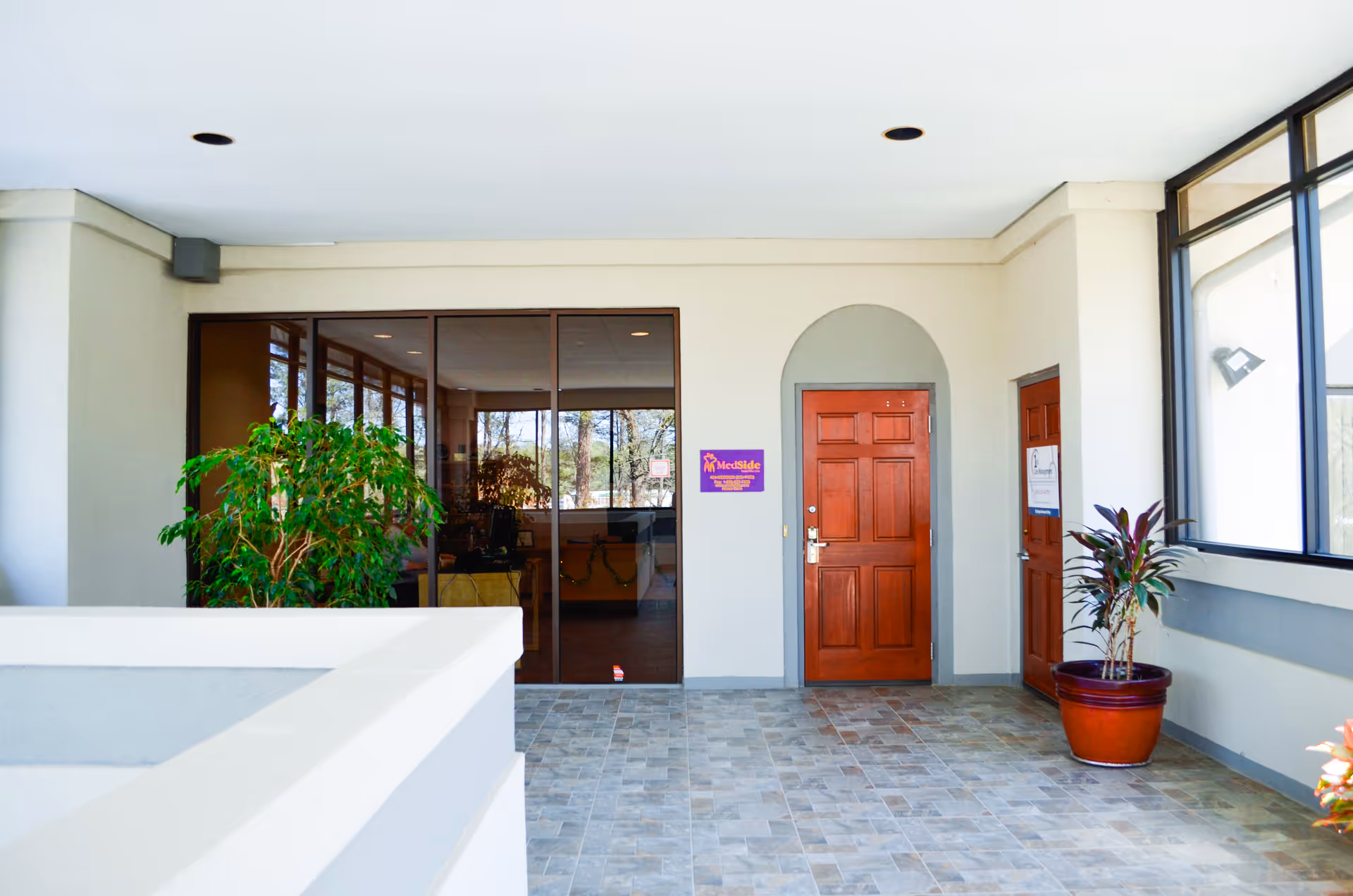 Medside Healthcare entrance: covered area with glass doors, potted plants, and tiled floor.