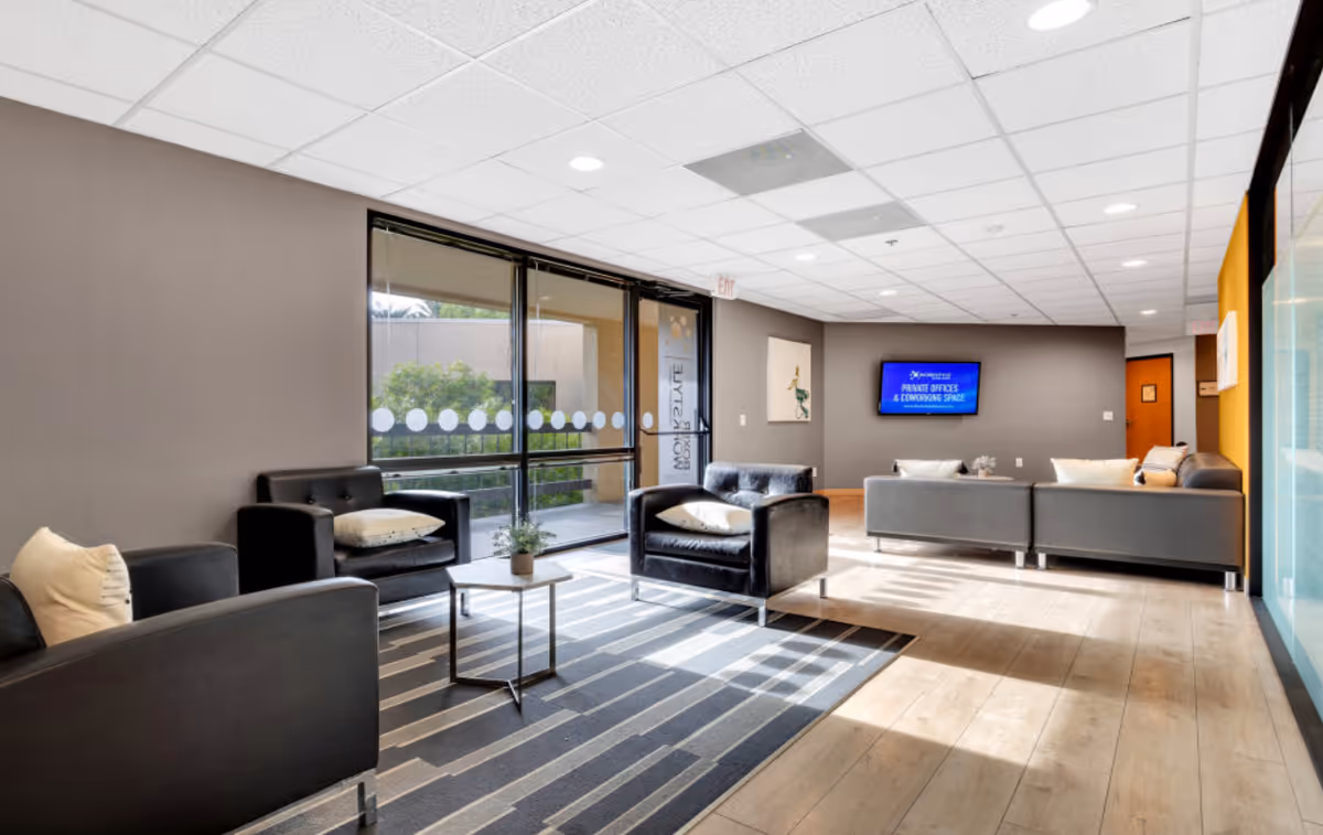 Modern interior lounge area with black leather seating, rug, glass doors, and a wall TV.