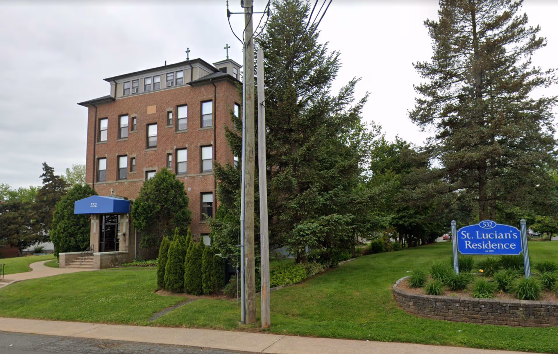 Brick senior residence building with blue entrance awning and landscaped front yard.
