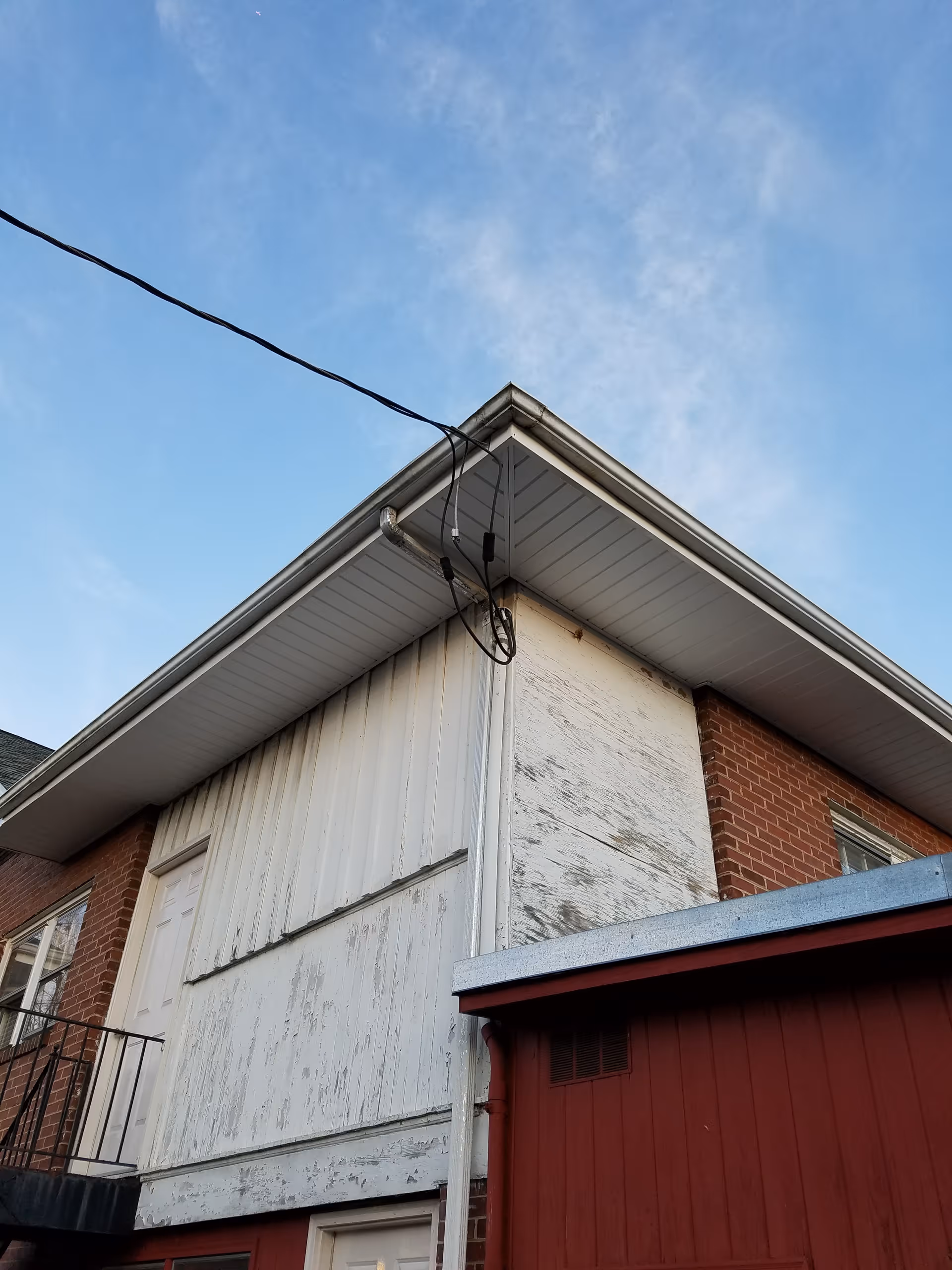 Exterior view of a brick and white siding building with a door and peeling paint.