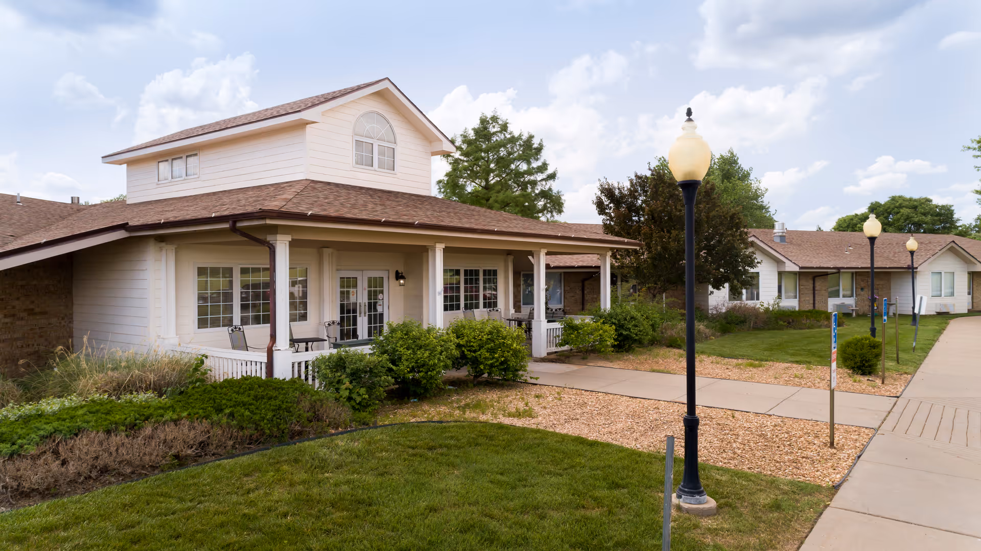 Exterior view of a single-story residential health building with a covered porch, landscaped lawn, sidewalks, and lampposts.