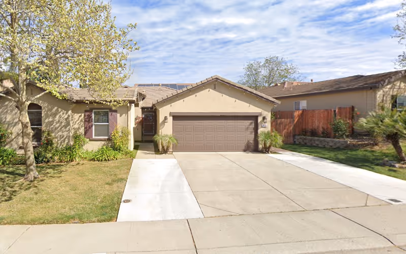 Single-story beige senior living facility with garage, driveway, and front yard on a sunny day.