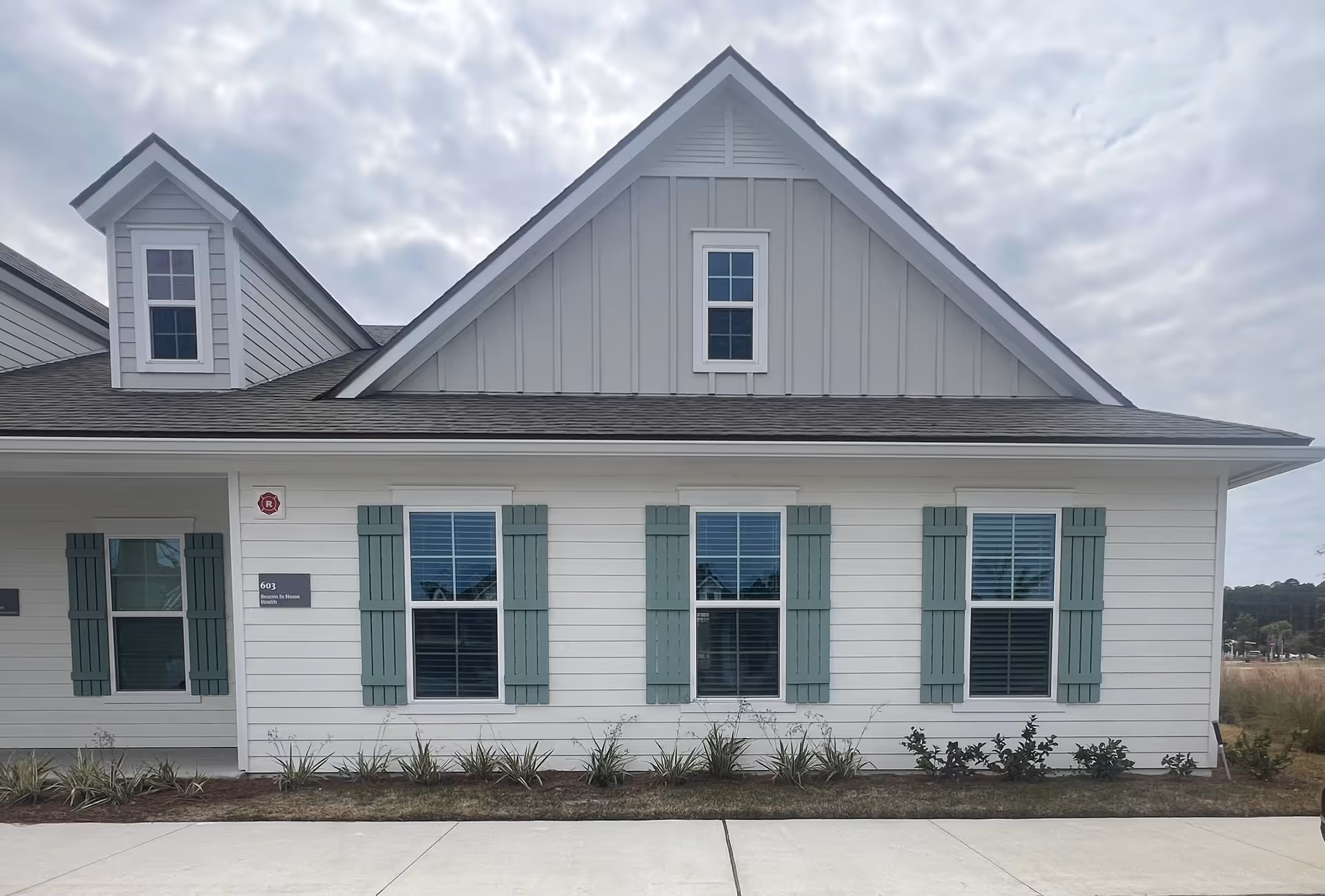 White siding building with green shutters and a gabled roof, front exterior.