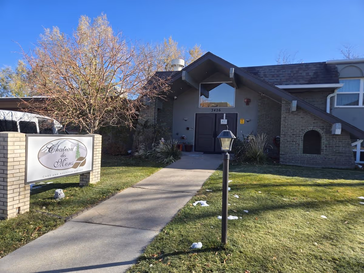 Front entrance of the Chateau des Mons care and assisted living building with a walkway, sign, lamp post, and a leafless tree.