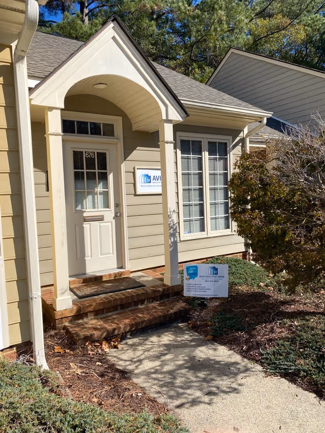 Front entrance of a beige building with archway, steps, and Avid Health at Home sign.