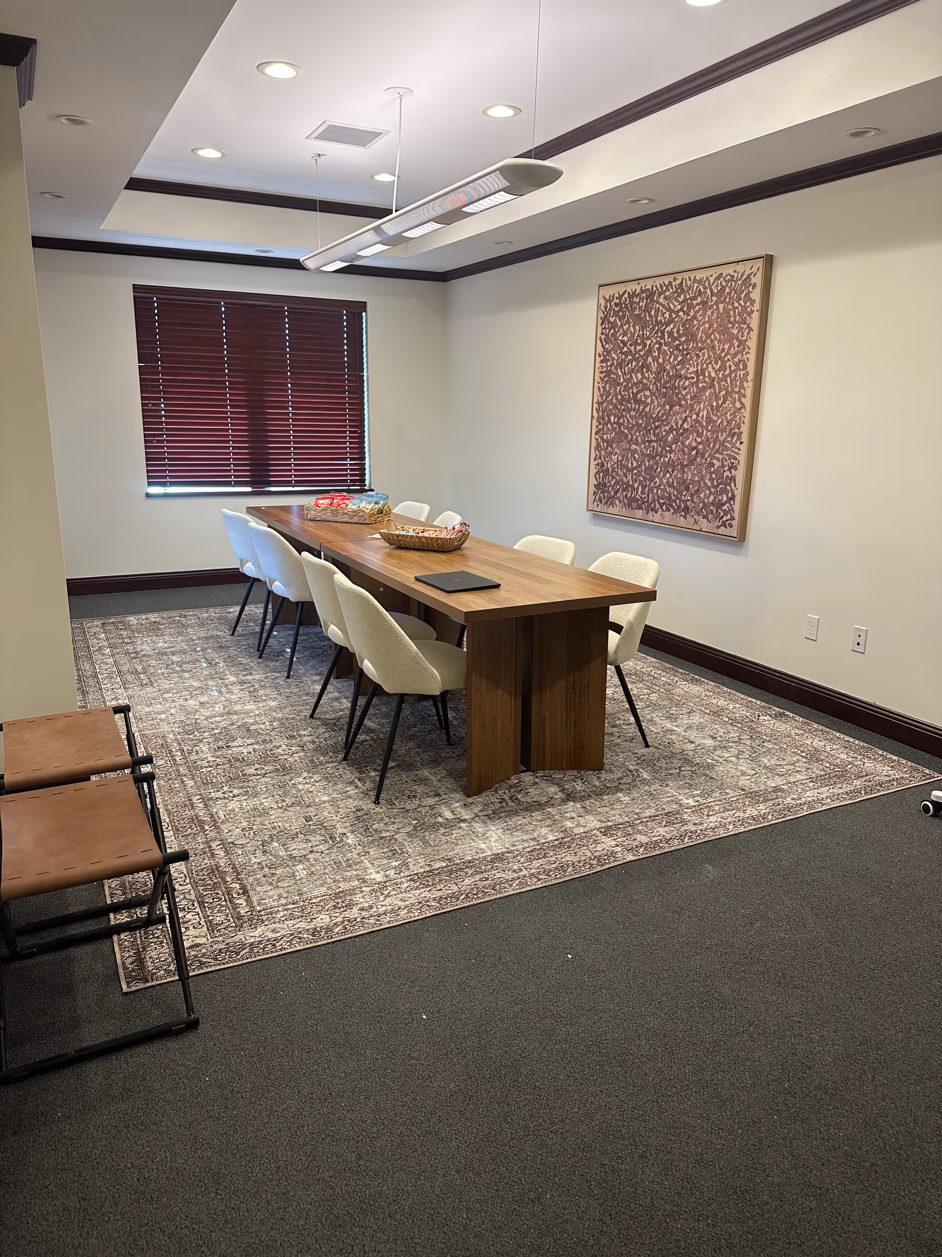 A long wooden dining table with white chairs in a well-lit, modern meeting room.
